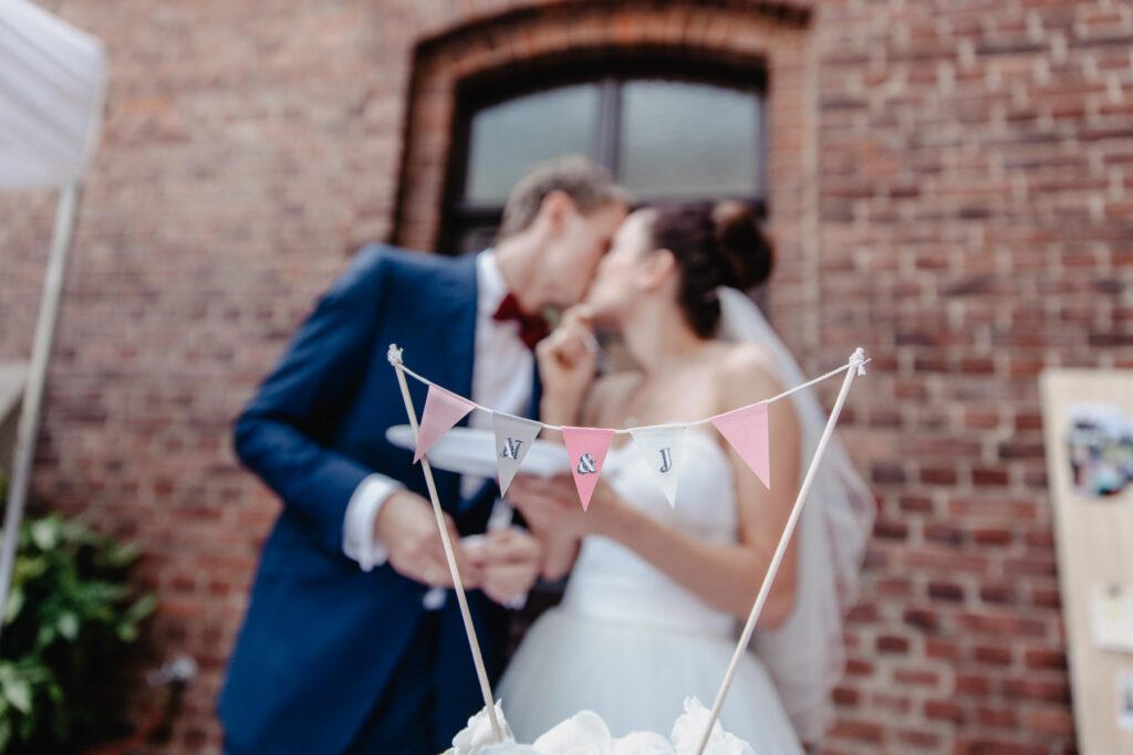 Wimpelkette mit den Initialen des Brautpaares auf einer Hochzeitstorte. Im Hintergrund das Brautpaar unscharf