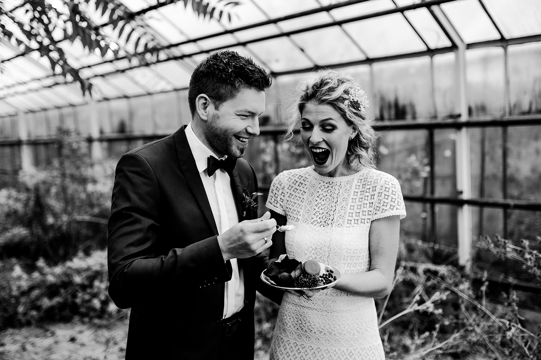 Herbsthochzeit – Lachendes Brautpaar isst Hochzeitstorte in einem Gewächshaus